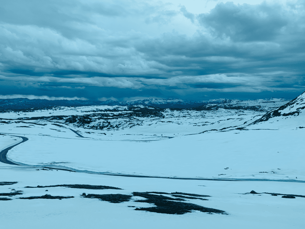 Driving in glacial elevations on Beartooth Highway with a winding road and snow covered mountains in the background