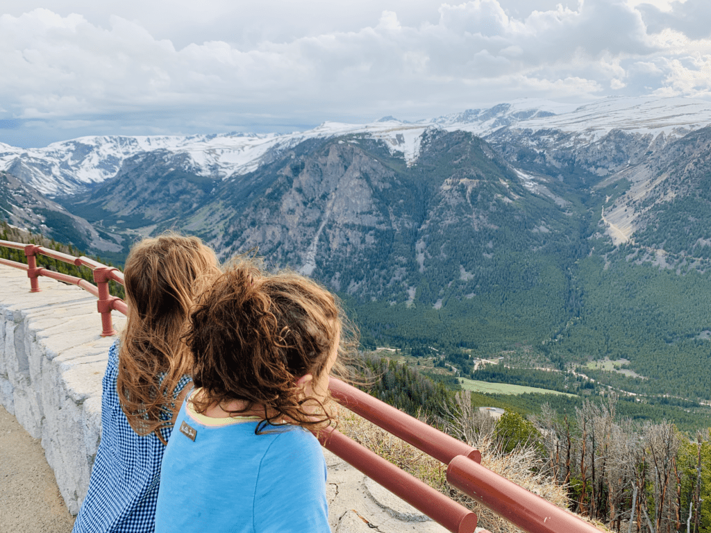 Girls looking out at the grand summit of Beartooth Pass with snowcapped summer mountains