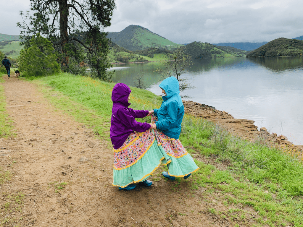 Two girls dancing together with serene lake and dog walking man in the background