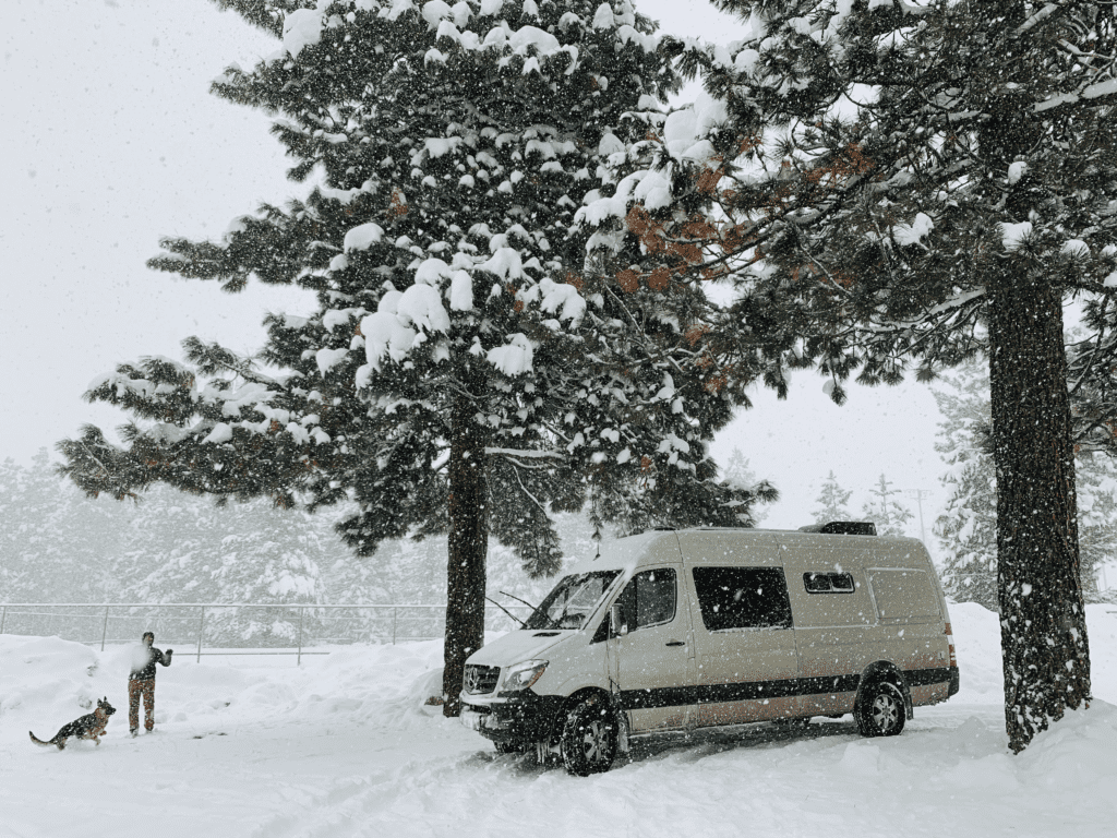 A man playing with his dog during a light snowfall in Tahoe living Van Life