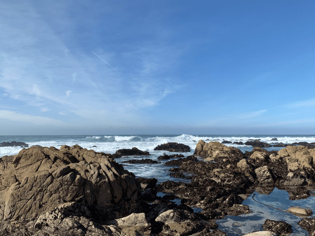 Blue skies with waves crashing on rocks at Asilomar State Beach