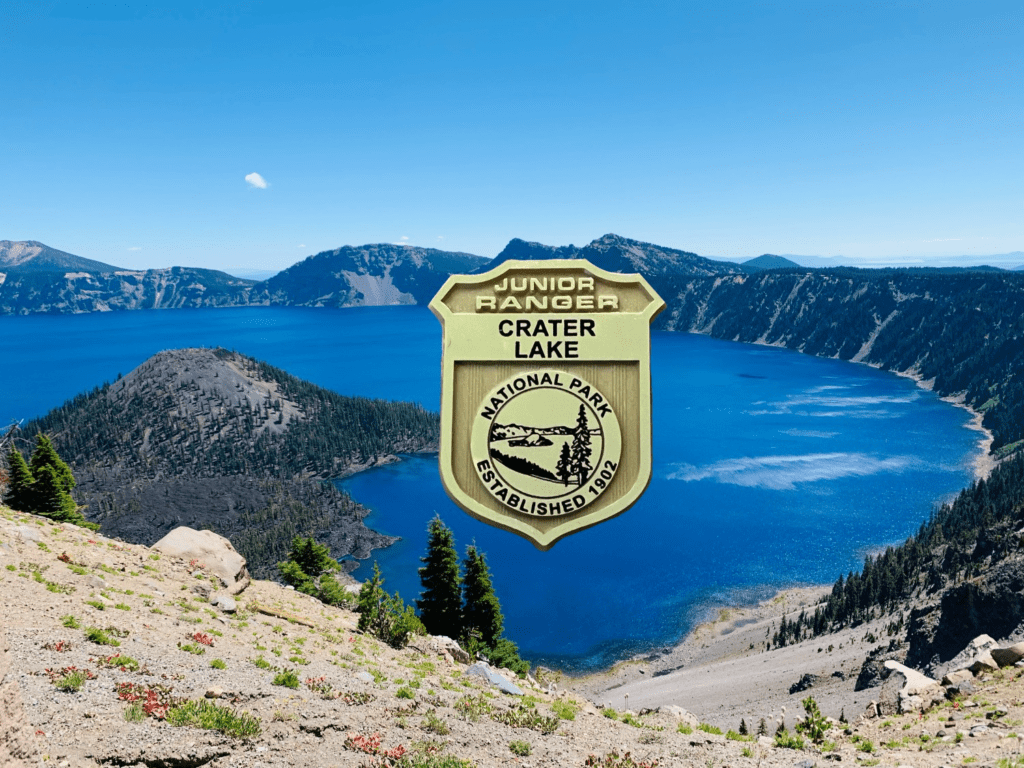 Crater Lake National Park NFT Junior Ranger badge with deep blue rim waters on rim of Crater Lake with Wizard Island in the background