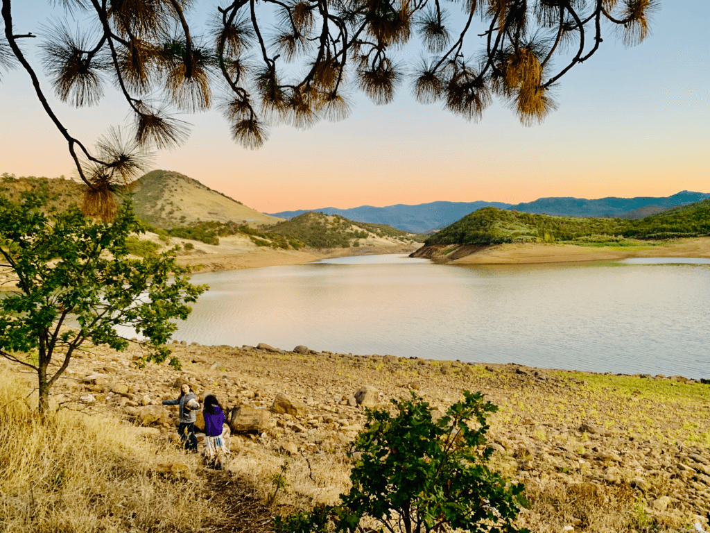 Kids Embracing dolls while surrounded by the yellow gold Harvest Essence of Still Water Emigrant Lake with red hue sunset in the background