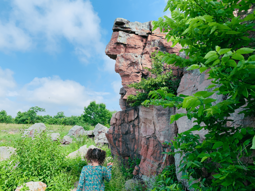 Girl at Pipestone National Park in Minnesota pointing at red rock with blue skies and white clouds in the background