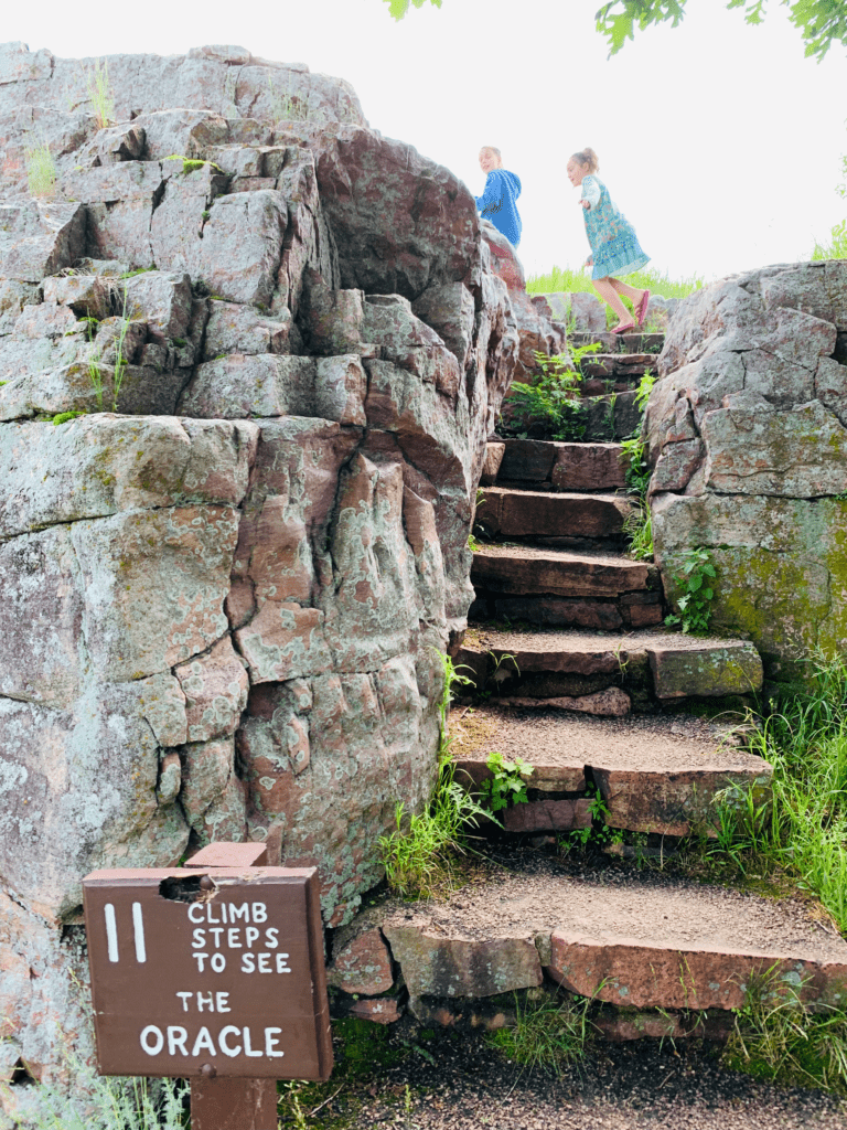 Happy kids climbing 11 red rock stairs to see the Oracle at Pipestone National Monument