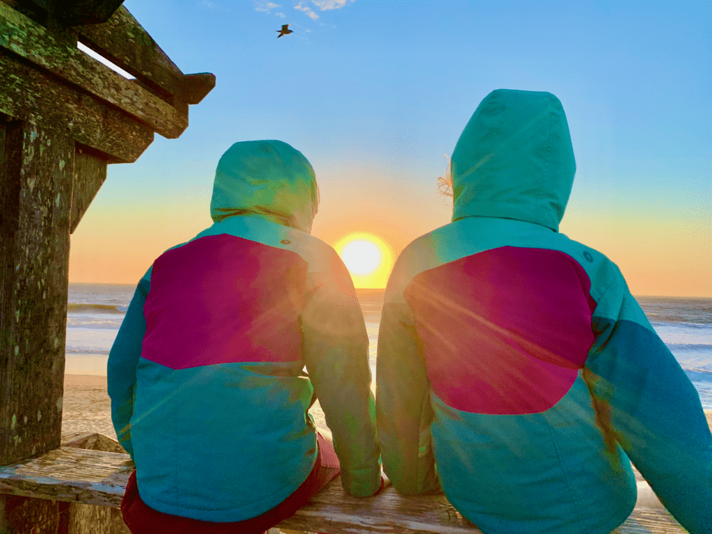 Sunset Between Us Sisters with sun rays hugging kids and rainbow sky in the background