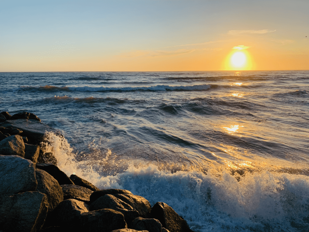 Blue waves crashing against rocks at Sunset Moss Landing State Beach with golden sunset in the background