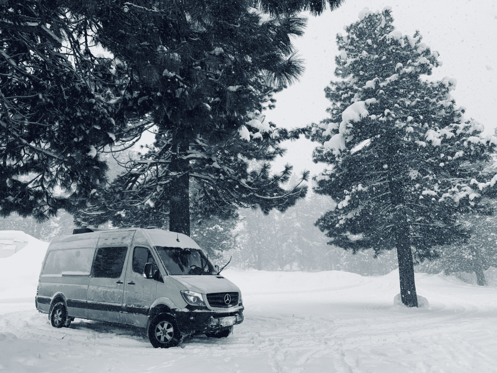 Van Life in Tahoe Winter Sprinter parked during a snowstorm with large conifers and snowflakes in the background