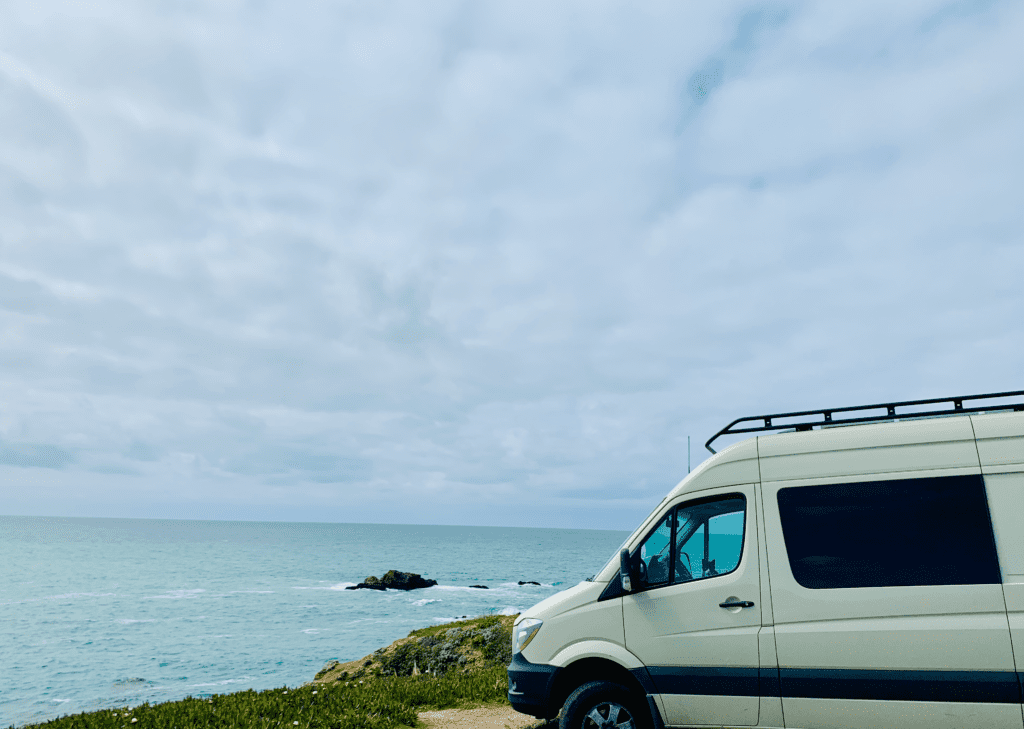 Van Life on the California Coast with Sprinter parked near gentle ocean waves and rock features in the background