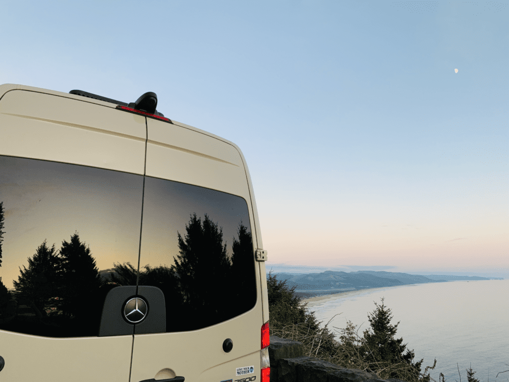 Van Life reflections in window with the Oregon coast with coastal trees and calm blue ocean water below a glowing moon in the background