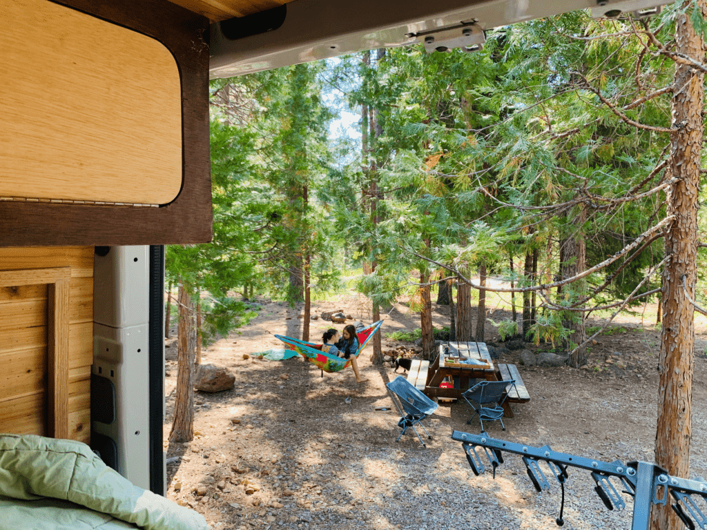 Van back doors open for fresh mountain air lazy summer days with kids in rainbow color hammock in the background