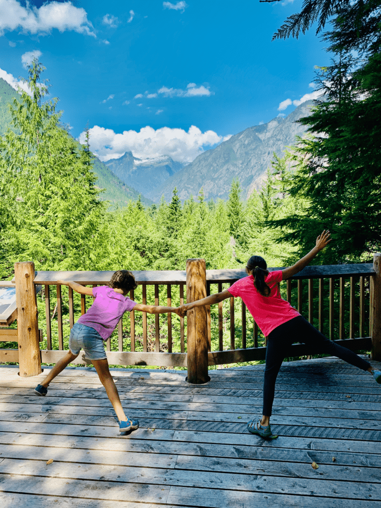 North Cascades Visitor Center Nature is Home kids dancing and holding hands with mountains and white fluffy clouds in background