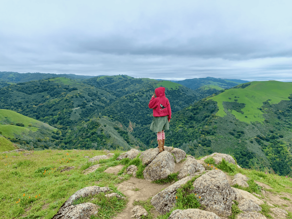 Kid hiking in freedom in the Midpeninsula Regional Open Space District that remains open during the covid-19 lockdown with green rolling hills and cloudy skies in the background