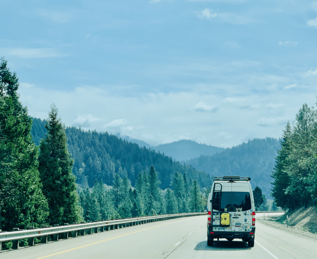 Oregon Van Life driving in the coastal ranges near Grants Pass Oregon with a yellow diesel fuel tank and hippie stickers on back of van with smoky skies in the background