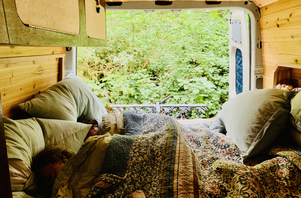 Kids Sleeping in Nature in the back van bed on the Oregon Coast with lush green plants in the background