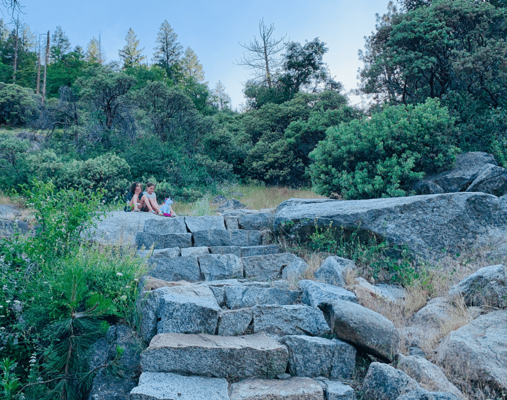 Granite Stairs to Heavenly View in Yosemite with our daughters and stuffed unicorn sitting near dark green trees and large granite boulders in the background