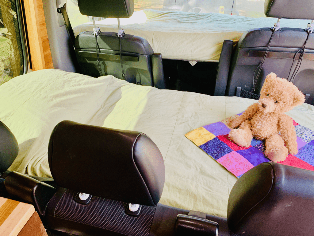 Van Double Bunk System suspended twin size beds hung from front and bench seats with green quilt and teddy bear on colorful doll quilt