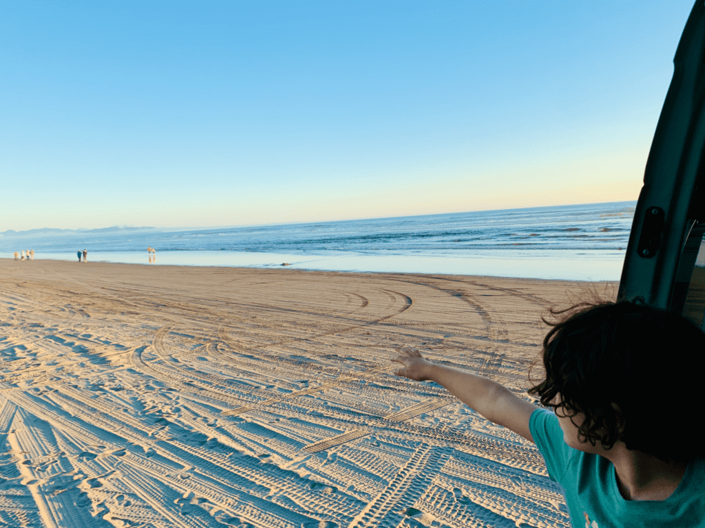 Van rescue Sons of Beaches at Fort Stevens State Beach in Oregon van kid pointing out at ocean with Pacific Ocean in the background