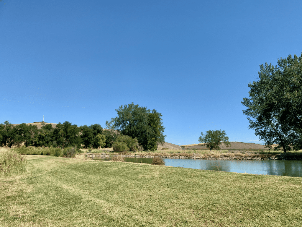 Whitman Mission Historic Site with Memorial on top of hill and lake and deciduous trees with clear skies in the background