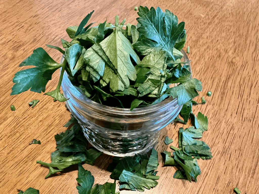 Fresh cut dark green parsley in a glass jar with wood kitchen in background