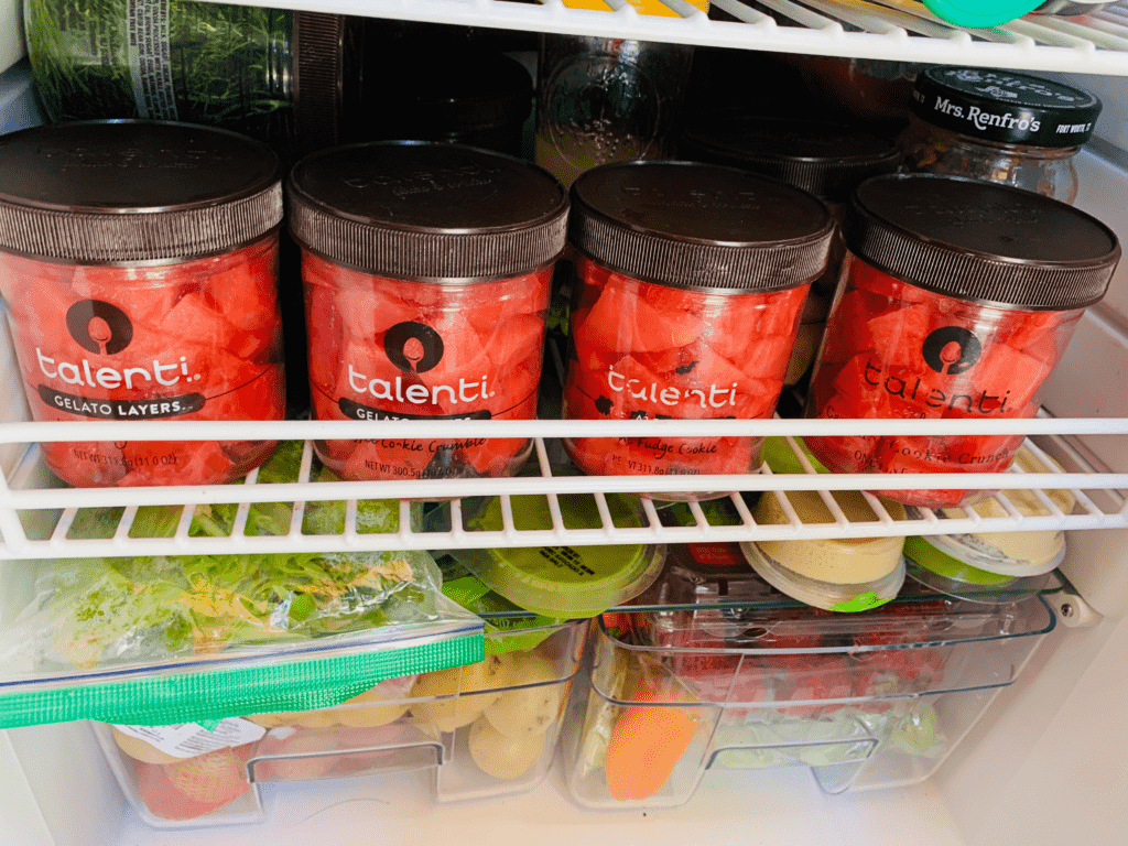 Talenti jars filled with red watermelon lined in a row in the van fridge with van fridge food in the background