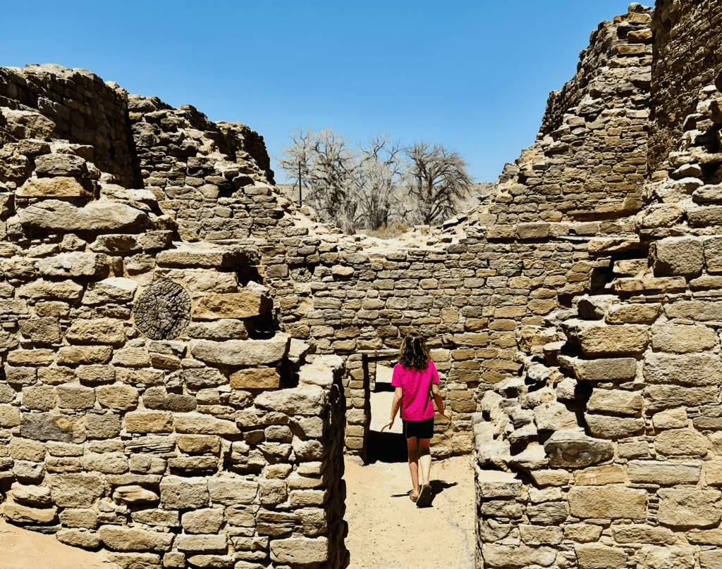 Junior Ranger on Aztec Ruins walking tour with ancient pueblo ruins and doorways in the background