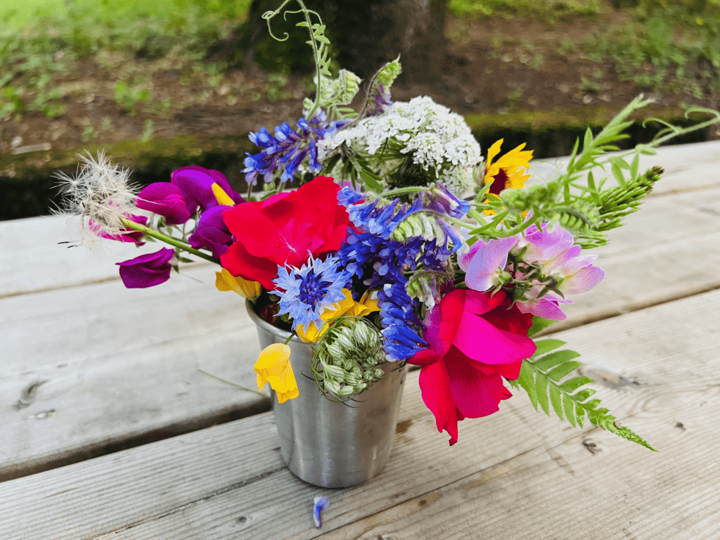 Colorful red yellow blue white purple flowers in a steel van kitchen cup sitting with picnic table in the background