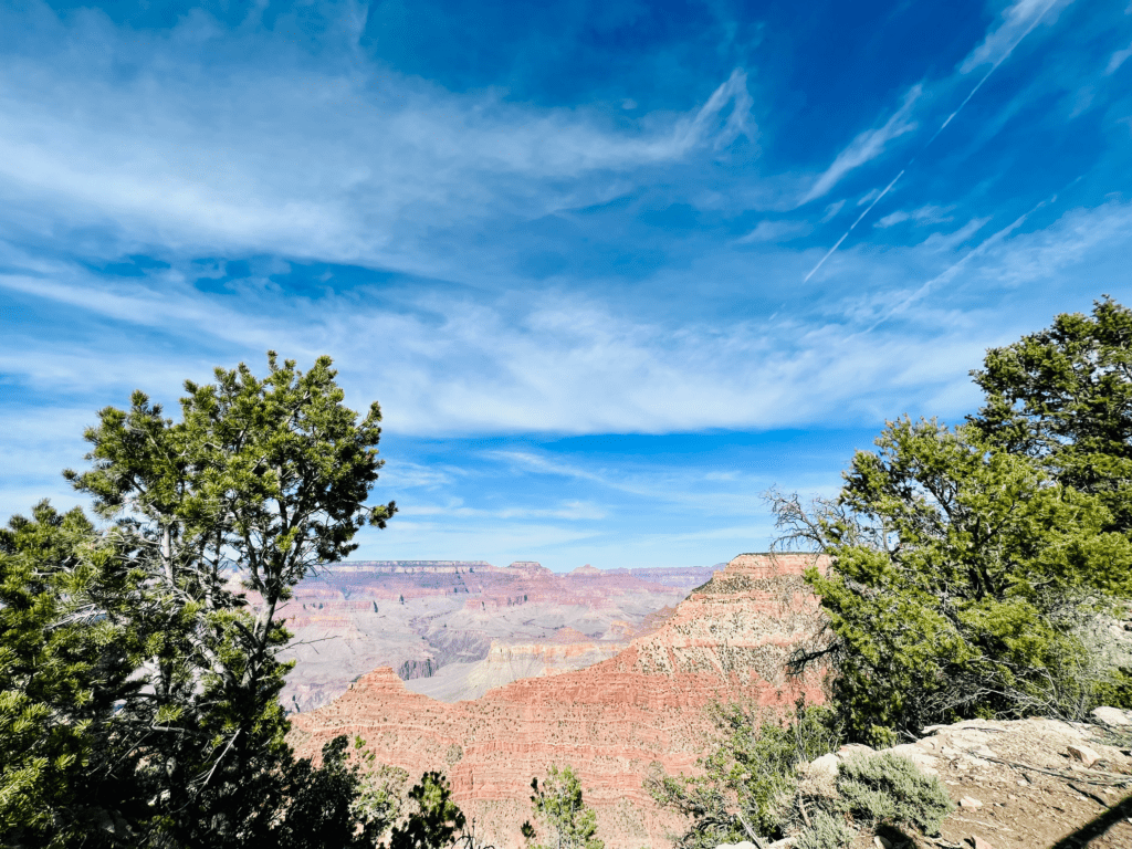 Grand Canyon South Rim with green trees and blue skies with wispy thin white clouds and colorful rock walls and canyons in the background