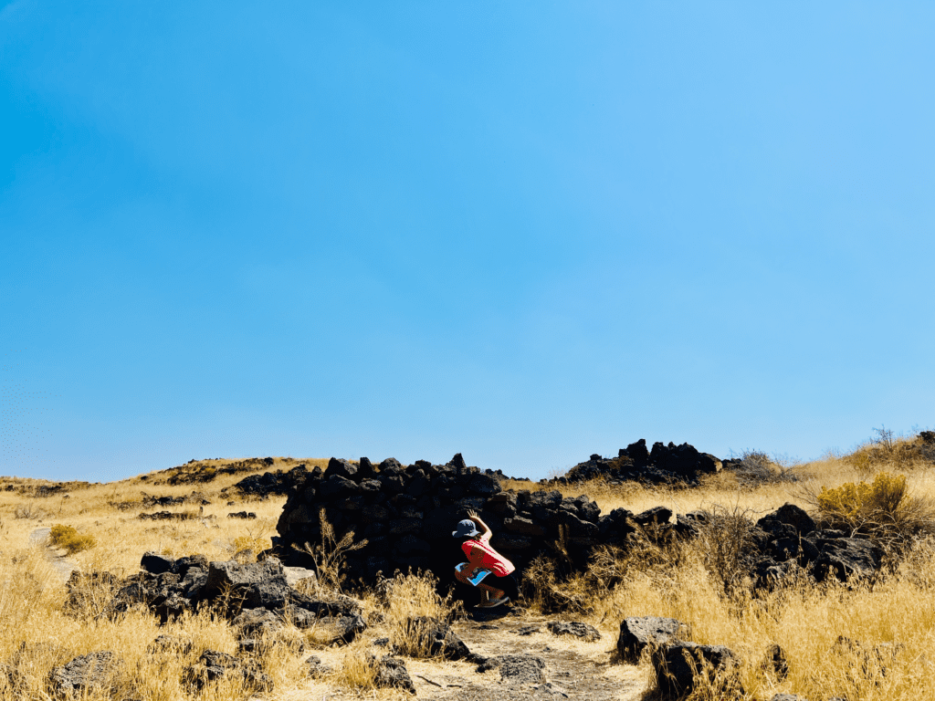 Our Junior Ranger Exploring the land of caves at Lava Beds National Park with igneous rock cave and clear skies in the background