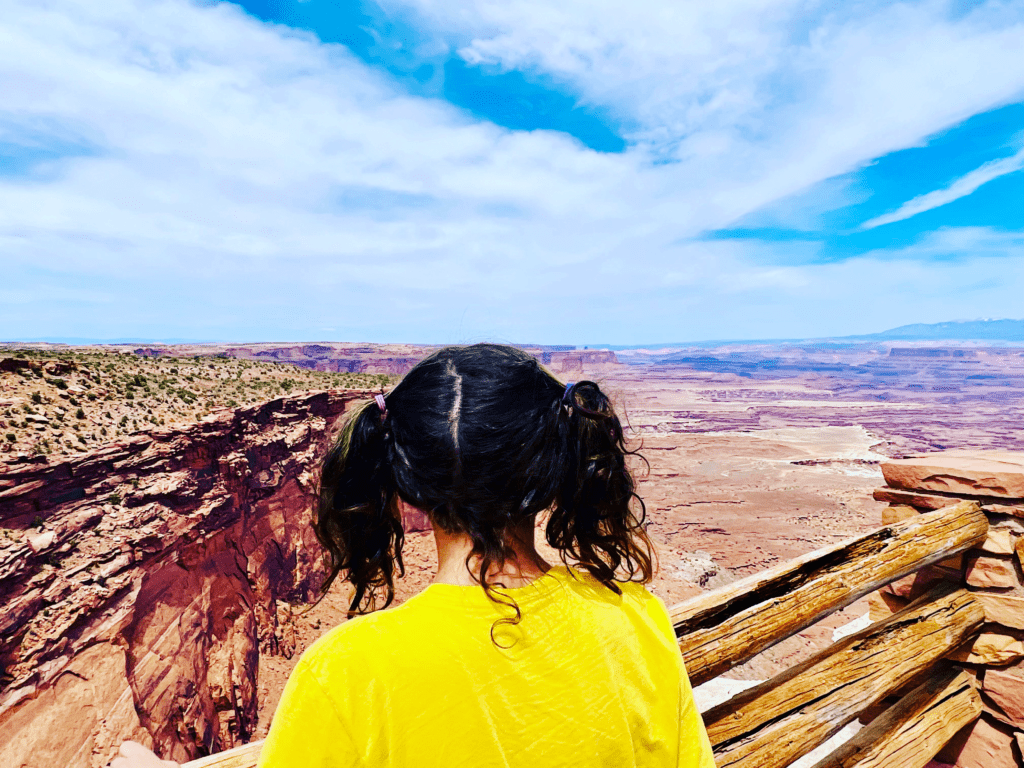 Phalen Happy Van Kid wearing bright yellow t-shirt and pic-tails in curly dark hair overlooking Canyonlands on scenic view point with miles of canyons in the background