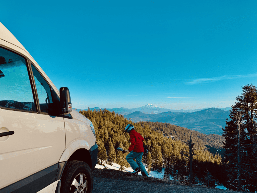 Van kid in ski jacket running next to Ski Van in the Siskiyou Mountains at Mount Ashland Ski Resort with Mount Shasta and Cascades view in the background