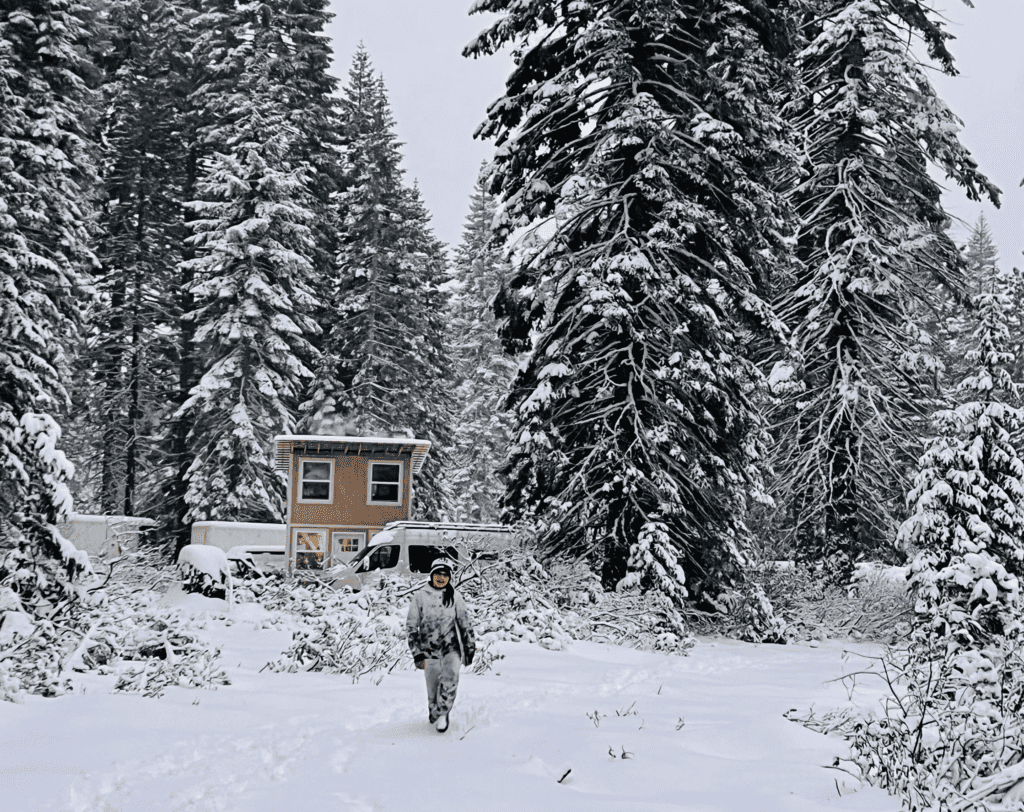 Mount Shasta Cabin in the winter with our older daughter happily playing in the snow with the cabin and van with towering snow covered white fir trees in the background